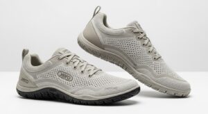 A pair of light grey Xero Shoes with mesh uppers, lace closures, and textured rubber soles. Designed for walking, they provide all-day comfort with ventilation holes and a minimalistic style. The "Xero" brand name is displayed on the shoes.