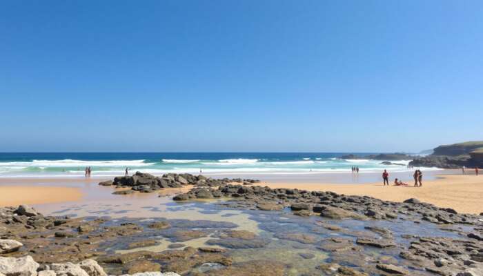 A sunny beach with clear waves, golden sands for sunbathing, rocky outcrops for exploration, accessible ramps, and diverse individuals enjoying the day under a blue sky.
